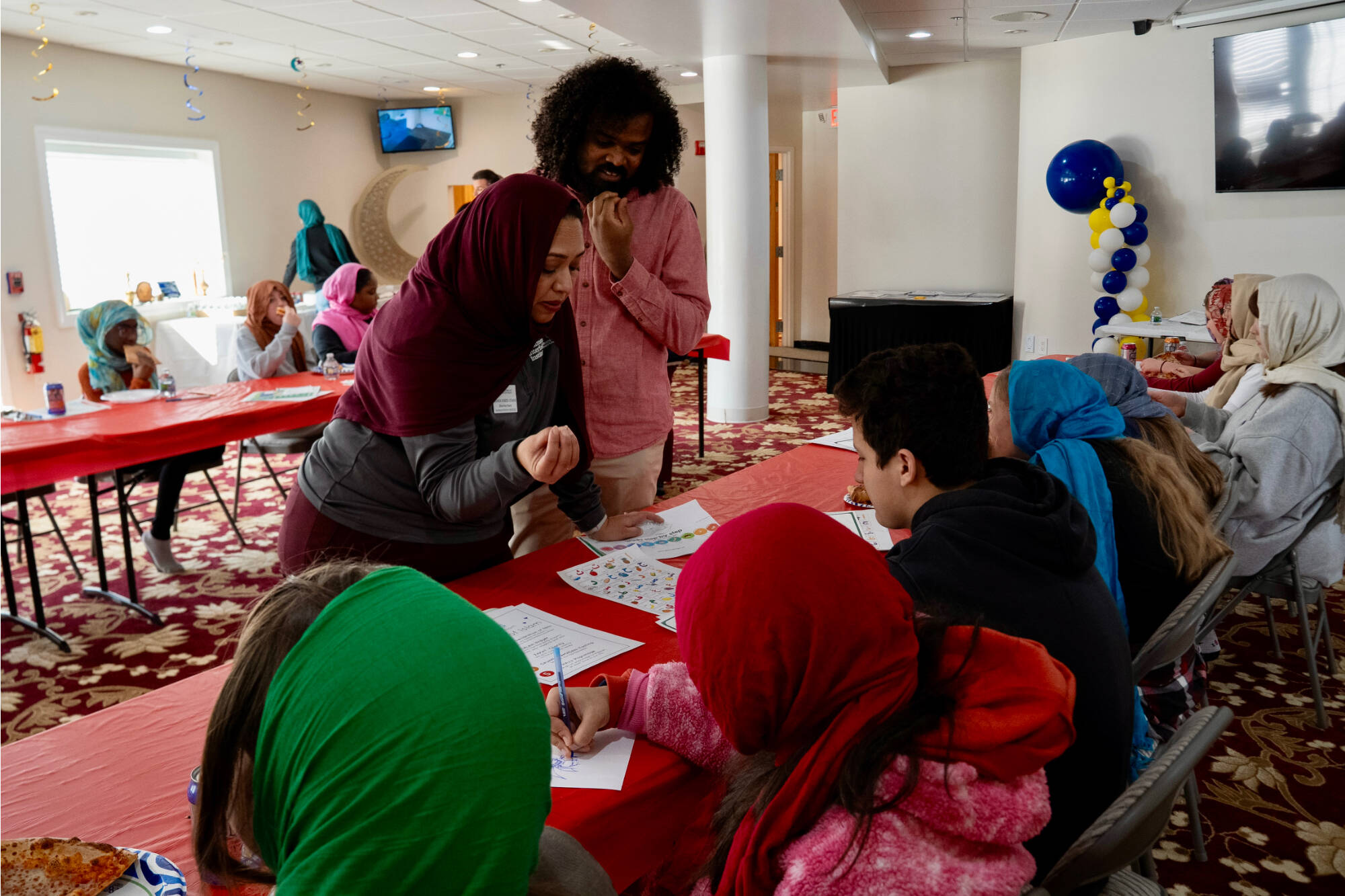 Two teachers leaning over a table describing an activity to students.